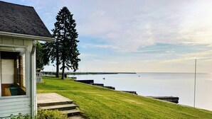 A house with a grassy yard, a dock, and a calm body of water in the background. - Lake Huron Cottage with Private Beach Access, walking distance to Port Sanilac (Port Sanilac)