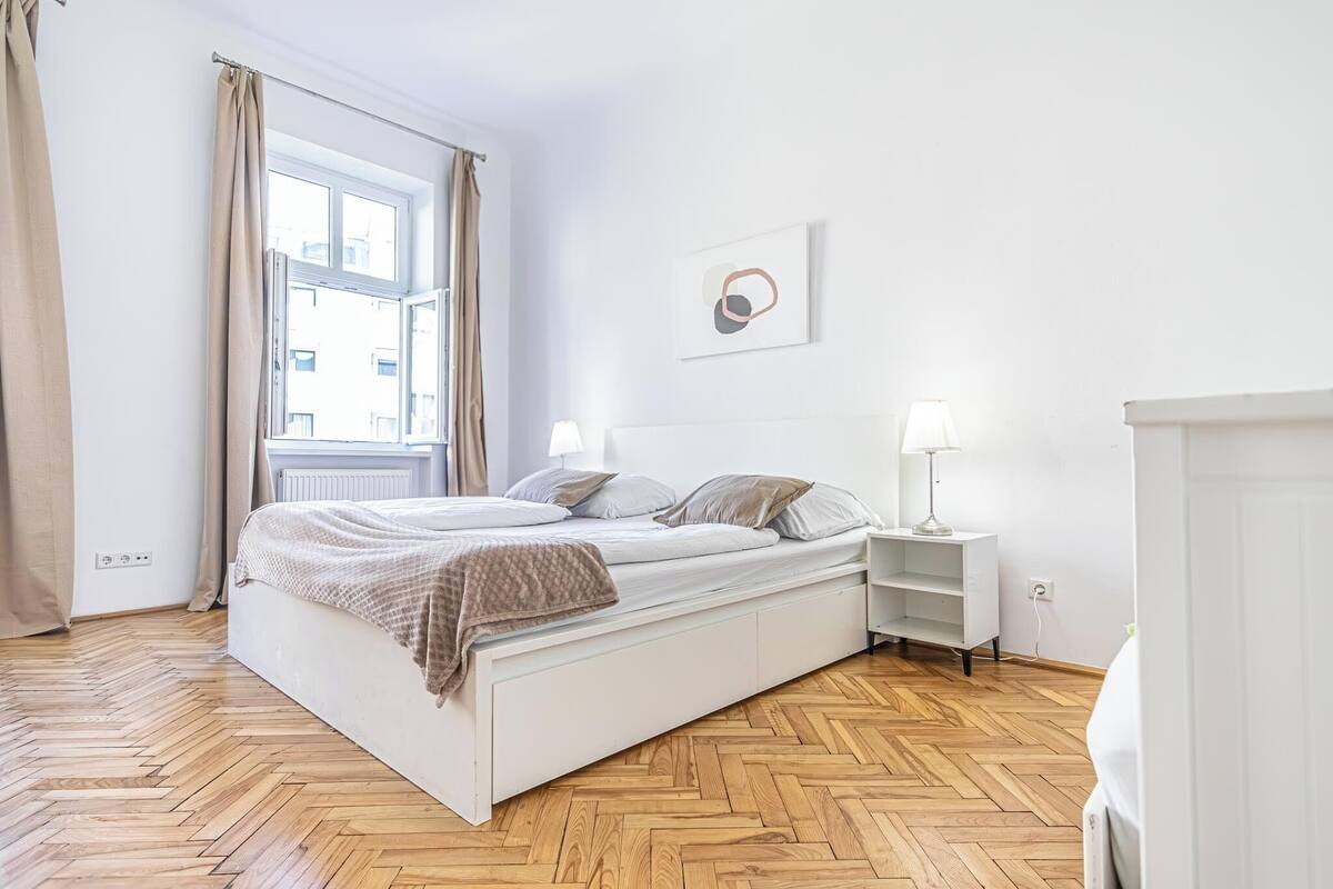 Un dormitorio con cama, mesitas de noche, una ventana con cortinas y un radiador.