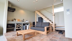 Un espacio habitable pequeño con kitchenette, un sofá, una mesa de centro de madera y una escalera.