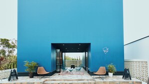 Un espacio al aire libre moderno con pared azul, dos sillas, una mesita y plantas en macetas.