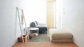 Una habitación pequeña y compacta con un sofá gris, un banco beige, una escalera y una mesita redonda con una cesta de alambre.