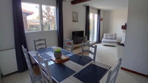 A dining area with a table, chairs, a potted plant, and a television in the background. - Large house in Provence village of Entressen with enclosed garden planted with trees, quiet location (Istres)
