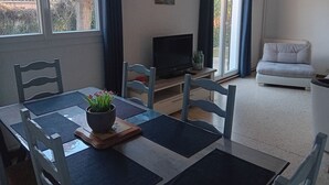A dining area with a table set for two, a television on a stand, and a sofa in the background. - Large house in Provence village of Entressen with enclosed garden planted with trees, quiet location (Istres)