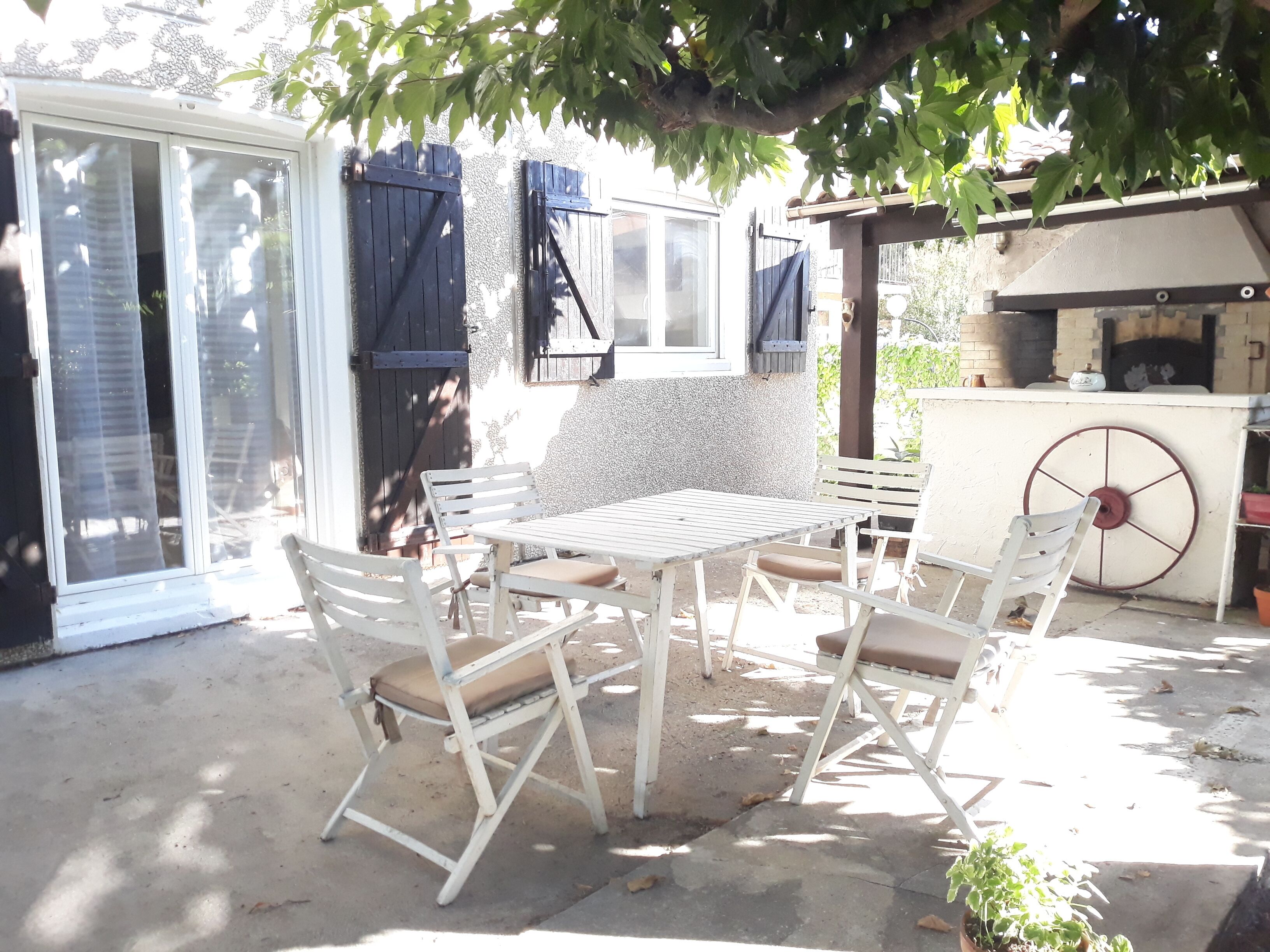 An outdoor patio with a table and chairs, a grill, and a covered seating area.