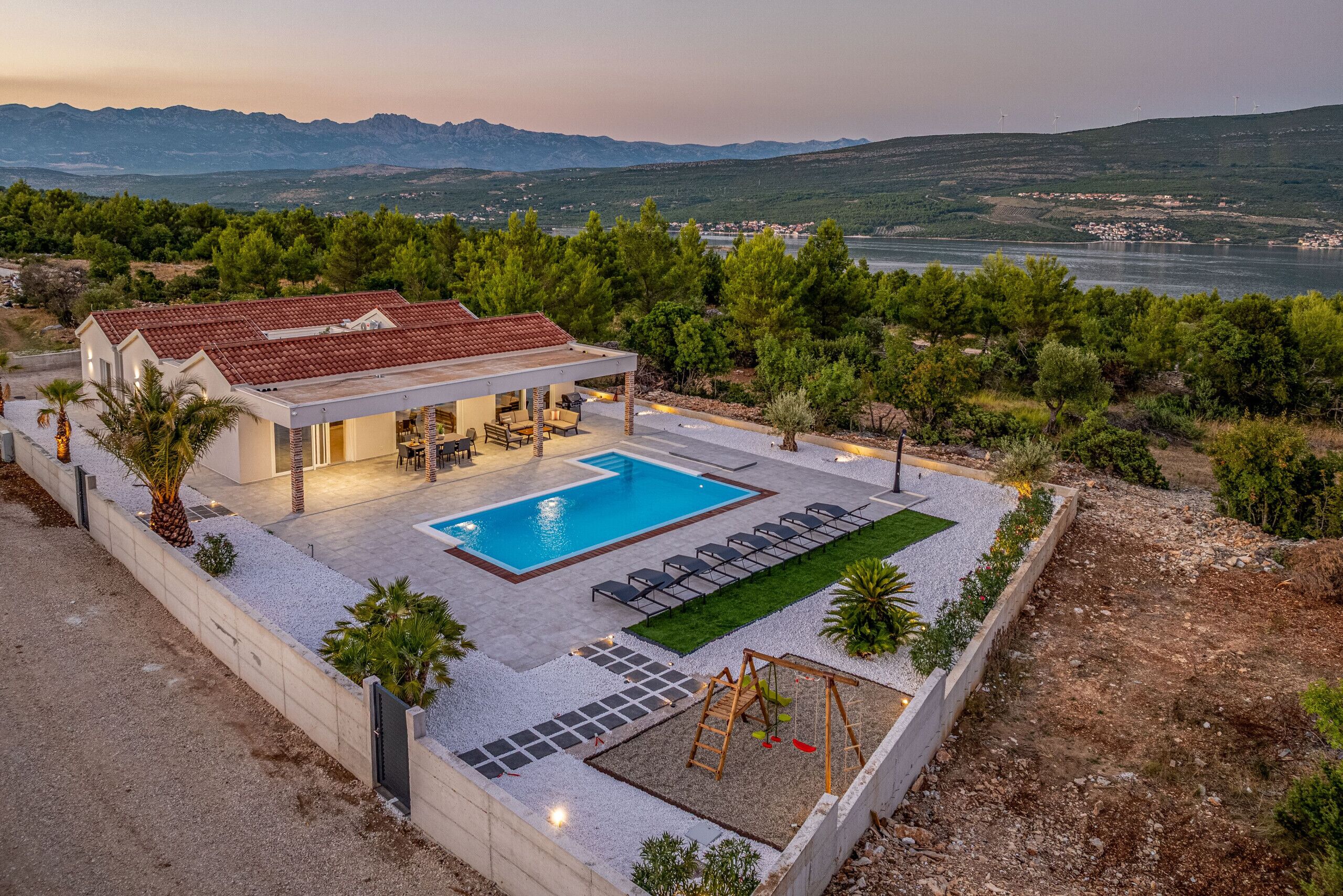 Une maison moderne dotée d’une piscine, d’un espace salon extérieur et offrant une vue sur les montagnes et la mer.