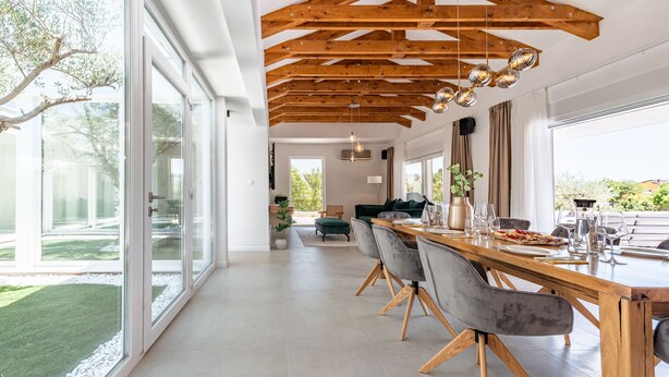 Un espace repas moderne avec un plafond en bois, de grandes fenêtres et une longue table dressée pour le dîner.