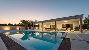 Et moderne poolområde med terrasse, siddepladser og et overdækket område.