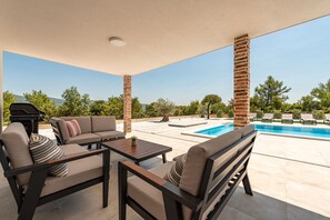 Ein überdachter Außenbereich mit Pool, Sitzgelegenheiten und Grill.