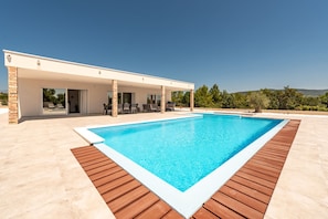 Ein modernes Haus mit Swimmingpool, überdachter Terrasse und Blick auf die Landschaft.