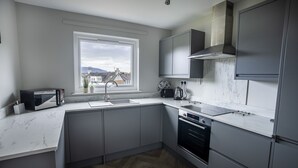 Et moderne køkken med lysegrå skabe, en hvid bordplade, indbygget ovn og et vindue med udsigt over bybilledet.