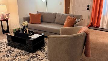 A living room with a sofa, armchair, coffee table, lamp, and a door with curtains.