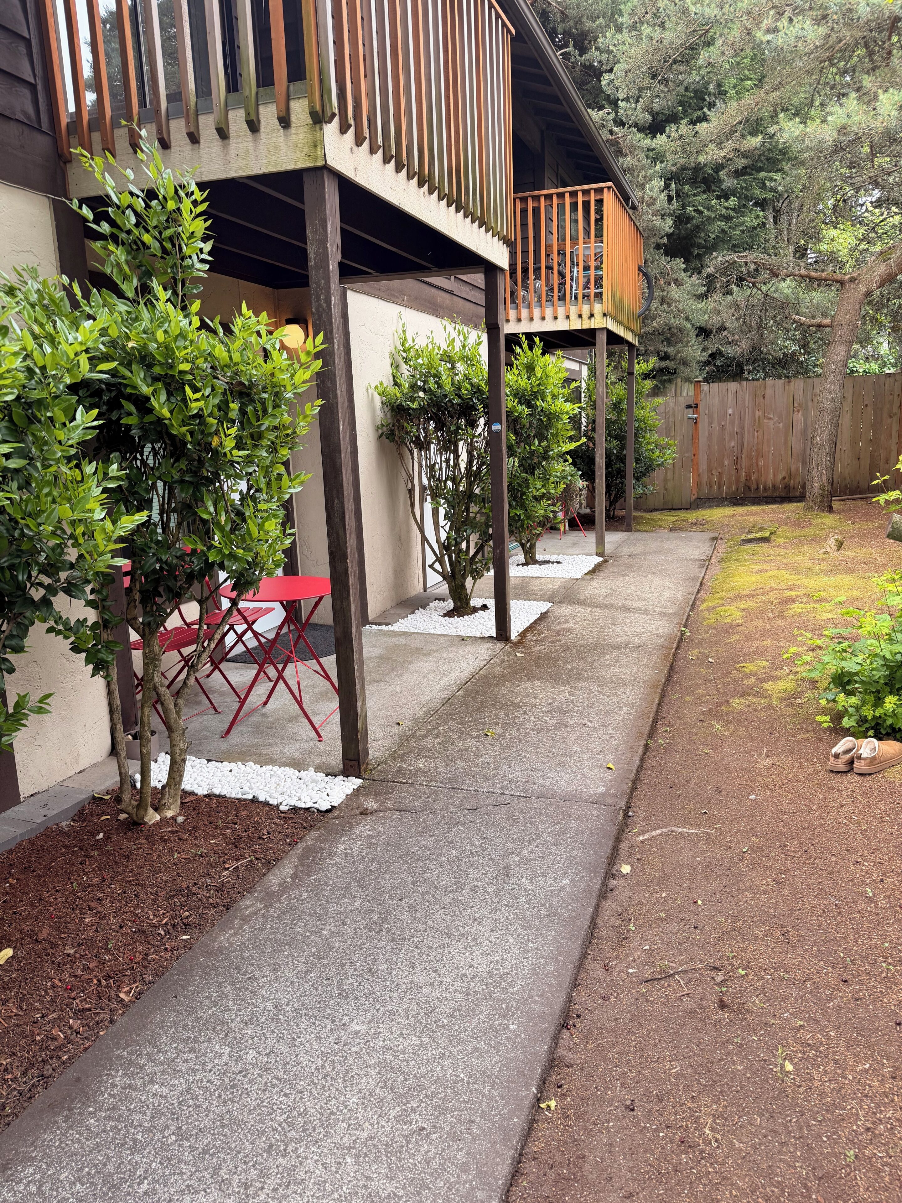 A covered outdoor patio with a concrete walkway, red folding chairs, and small trees.