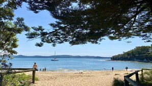 A beach with a sandy shore, a sailboat in the water, and people walking along the beach. - Pool, stroll to beach and cafe (PEARL BEACH)