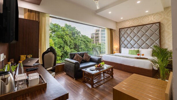 A modern hotel room with a large bed, a sofa, a coffee table, and a TV. - Aliste millennium City centre, Fortis, Gurugram (Gurugram)