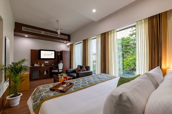 A hotel room with a large bed, a desk, a chair, a TV, and a window with curtains.
