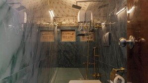 A bathroom with a marble wall, a toilet, a shower with a glass door, and a towel rack. - Shamiyana by Stay Serene Luxury (Murbad)