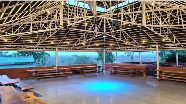 A covered outdoor area with a wooden floor, benches, and a metal roof structure. - Shamiyana by Stay Serene Luxury (Murbad)