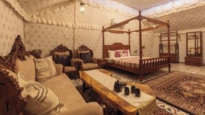 A traditional four-poster bed with a canopy, a sofa, a wooden coffee table, and a patterned rug in a room with patterned wallpaper and a ceiling fan. - Shamiyana by Stay Serene Luxury (Murbad)