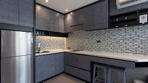Une cuisine moderne avec des meubles de couleur sombre, un réfrigérateur en acier inoxydable, un dosseret carrelé et un coin bar avec des tabourets.