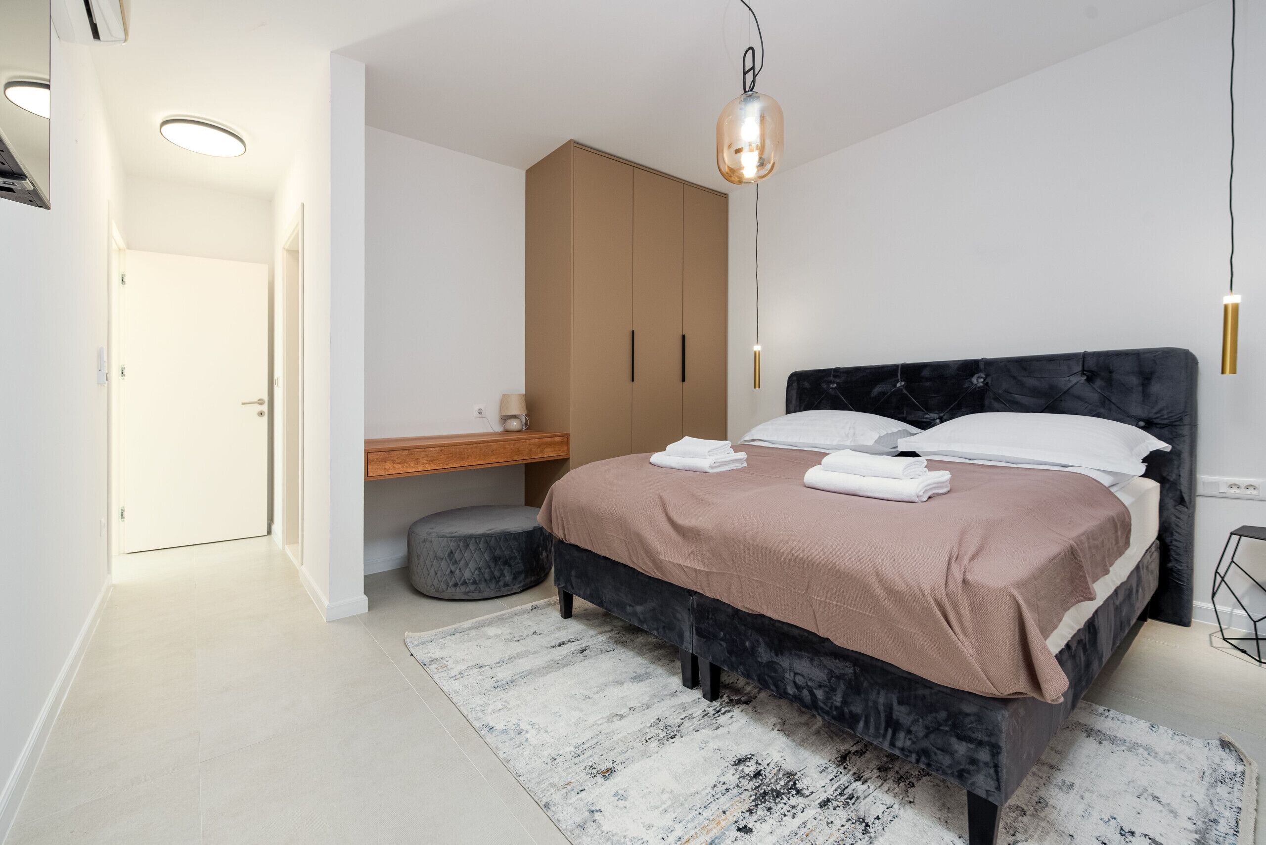Um quarto moderno com uma cama grande, uma mesa de cabeceira de madeira, um guarda-roupa e um lustre.