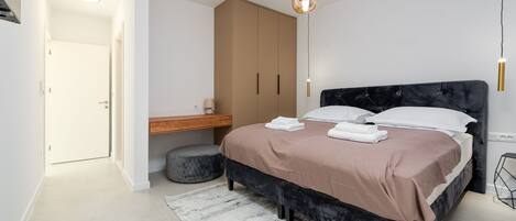 Um quarto moderno com uma cama grande, uma mesa de cabeceira de madeira, um guarda-roupa e um lustre.