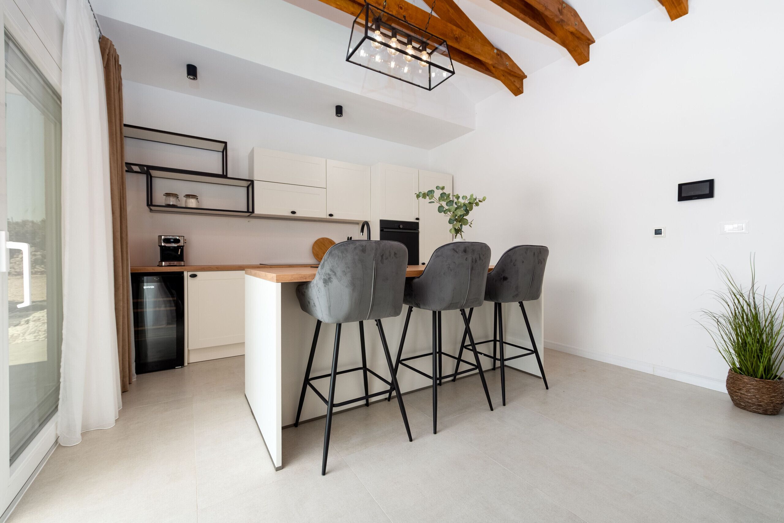 Una cocina moderna con encimera de madera, cuatro taburetes grises y una planta en maceta.