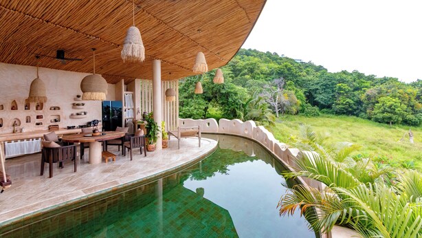 Un espace aménagé au bord de la piscine, avec une piscine aux formes arrondies, un plafond en bois et des lampes suspendues.