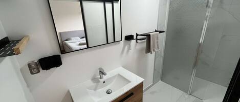 A modern bathroom with a white sink, wooden vanity, a large mirror, and a glass shower enclosure.