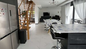 A modern kitchen with a wooden staircase, a dining area with a table and chairs, and a living room with a sofa and TV. - "Villa LOM: 800m from the beach (Asnelles)