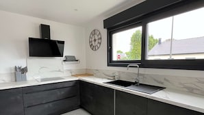 A modern kitchen with dark cabinetry, a white marble countertop, and a window with a view of the outside. - "Villa LOM: 800m from the beach (Asnelles)