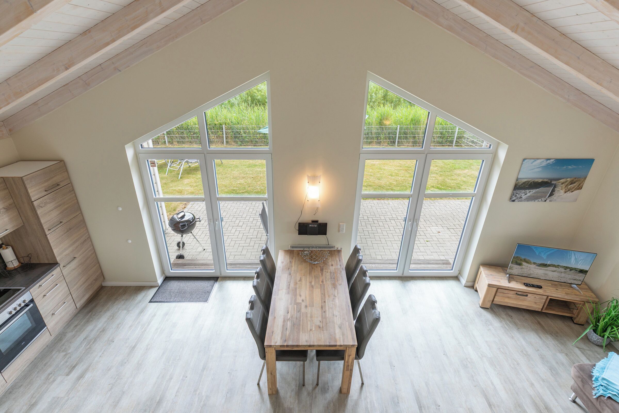 A modern kitchen with a wooden table and chairs, large windows, and a view of the outdoors.