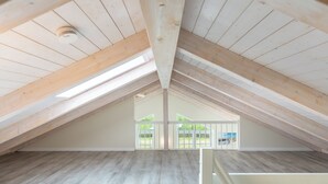 An attic room with wooden beams, a sloped ceiling, and a view of a backyard through large windows.