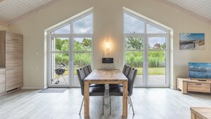 A spacious dining area with a wooden table and chairs, large windows, and a television on a wooden stand.