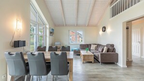 A spacious living room with a high ceiling, a dining area with modern chairs, a sofa, and a coffee table.