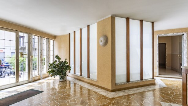 A spacious lobby with large windows, a potted plant, and a tiled floor.