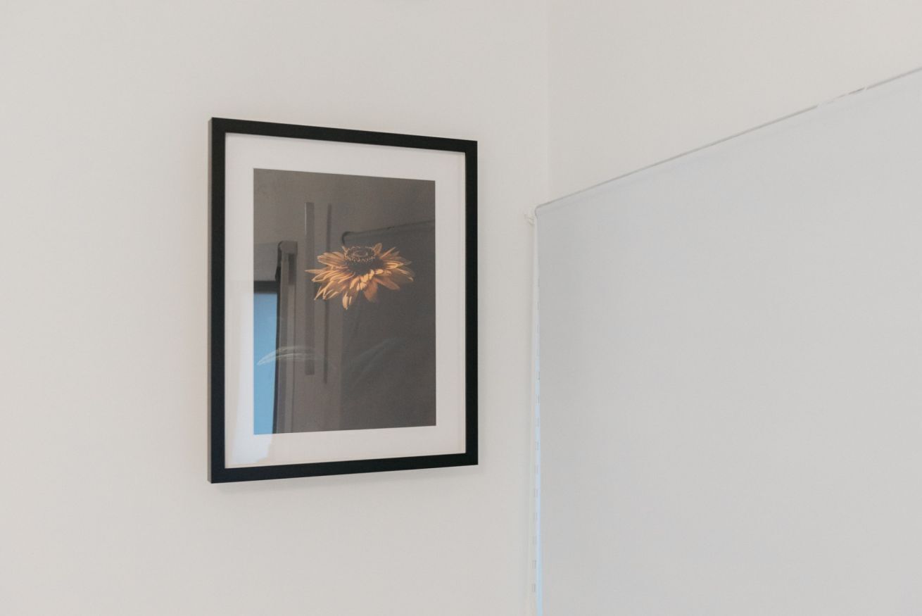 Ein gerahmtes Bild von einer Sonnenblume an einer weißen Wand.