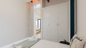 A bedroom with a bed, a green bedside table, a white wardrobe, and a mirror.