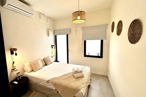 A hotel room with a bed, bedside table, lamp, air conditioning unit, window, and wall decorations. - Travel Habitat Playa del Cabanyal 1 (Valencia)