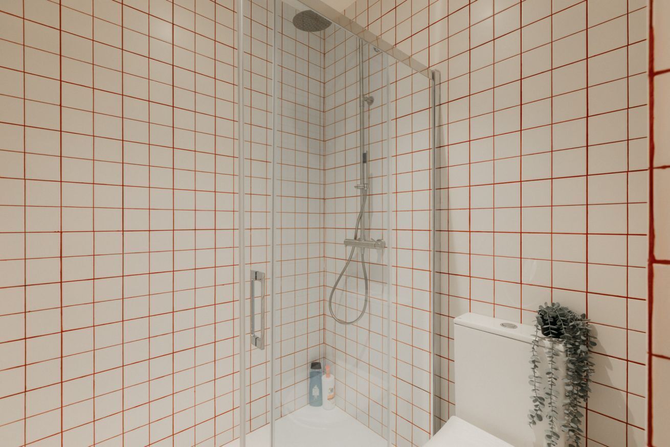 Ein kleiner, abgeschlossener Duschbereich mit Glastür, einer weißen Toilette und einer kleinen Pflanze an der Wand.