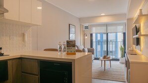 A modern kitchen with a built-in dishwasher, a dining area with a table and chairs, and a view of the city through large windows. - w* | Sunlit 1BR w/ Private Balcony in Miraflores (Miraflores)