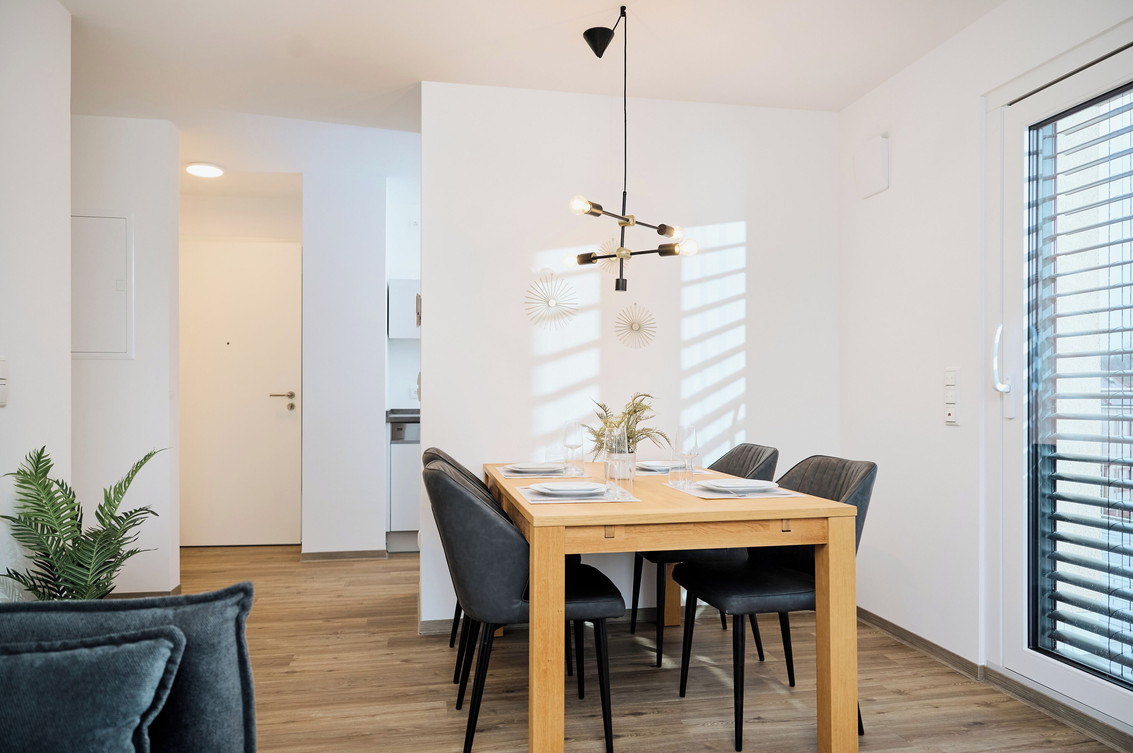Un espace repas avec une table en bois, des chaises noires et un luminaire suspendu.