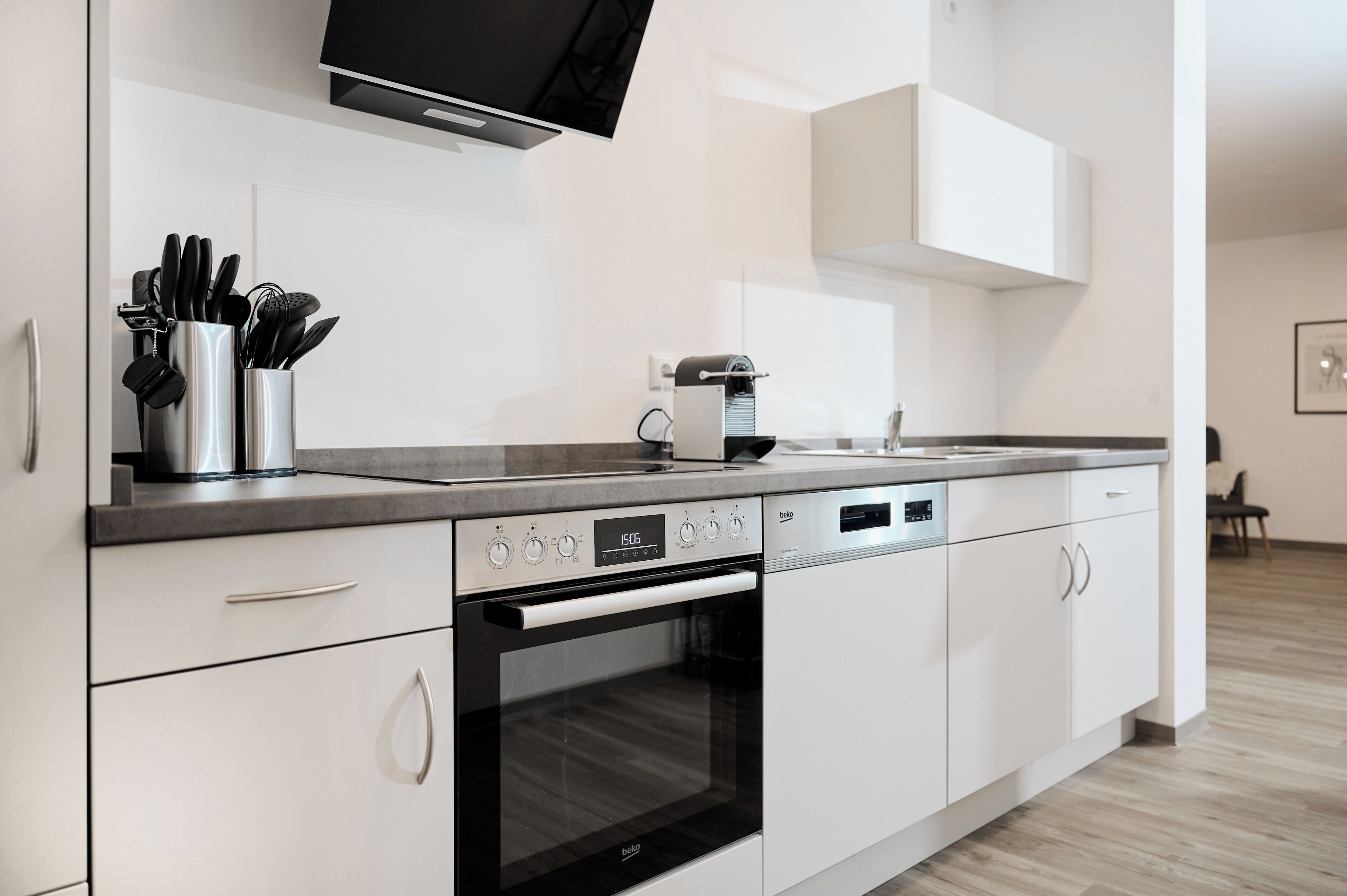 Une cuisine moderne avec des meubles blancs, un four encastré, une machine à café et un téléviseur à écran plat fixé au-dessus du plan de travail.