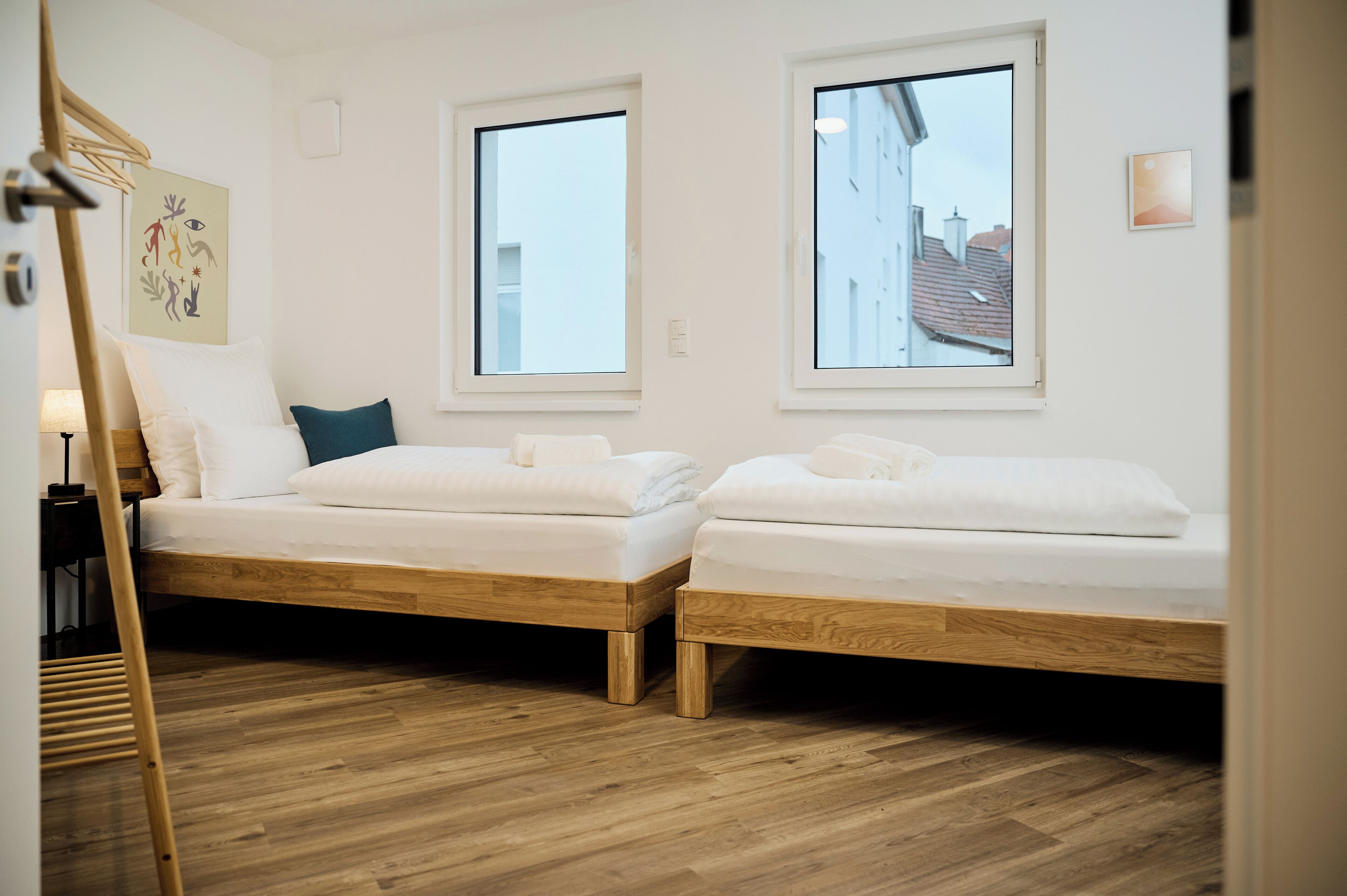 A room with two wooden beds, white bedding, and a wooden floor.