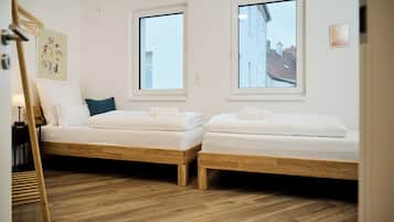 A room with two wooden beds, white bedding, and a wooden floor.