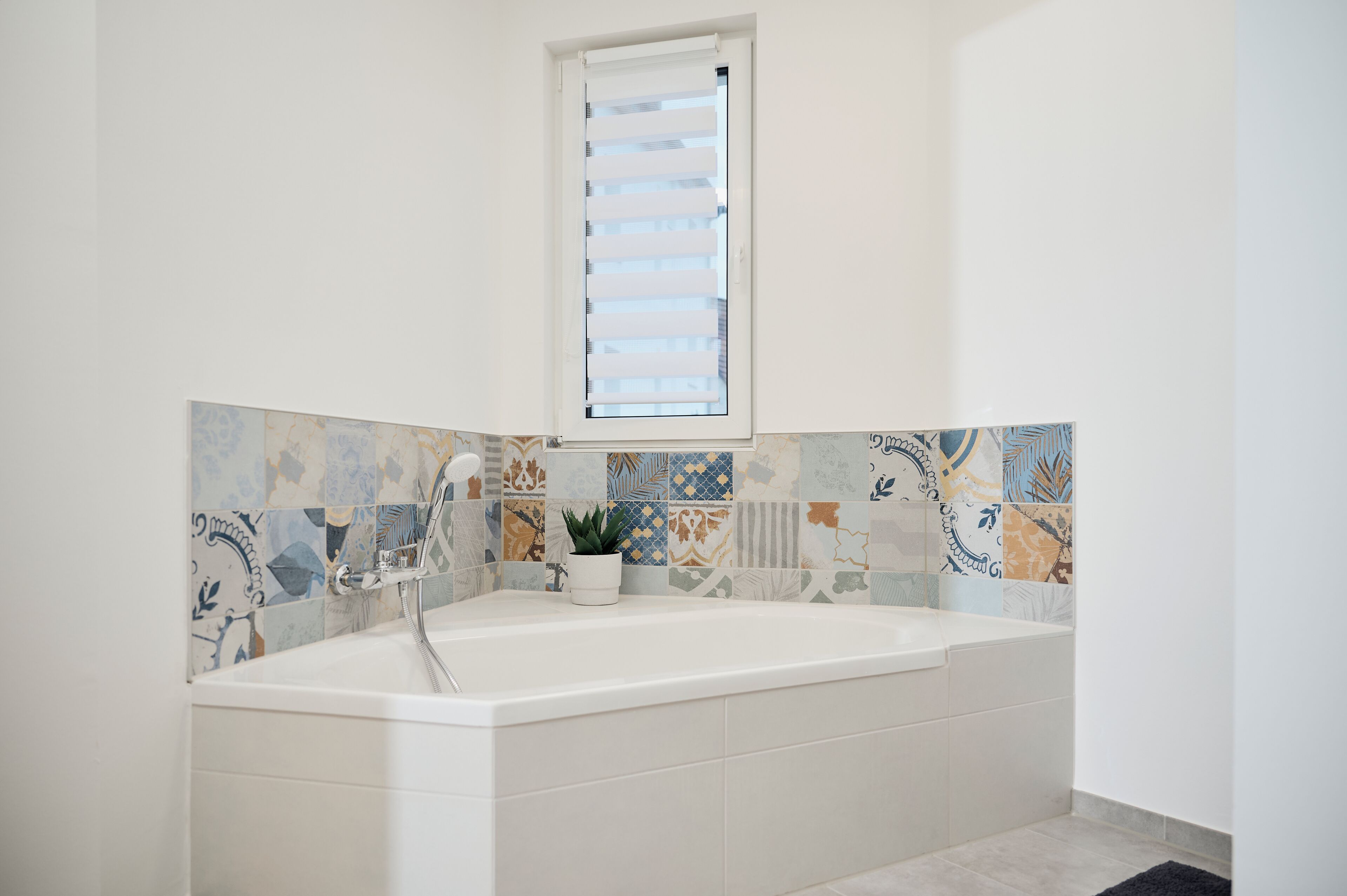 A bathroom with a bathtub, a window, and a tiled backsplash.