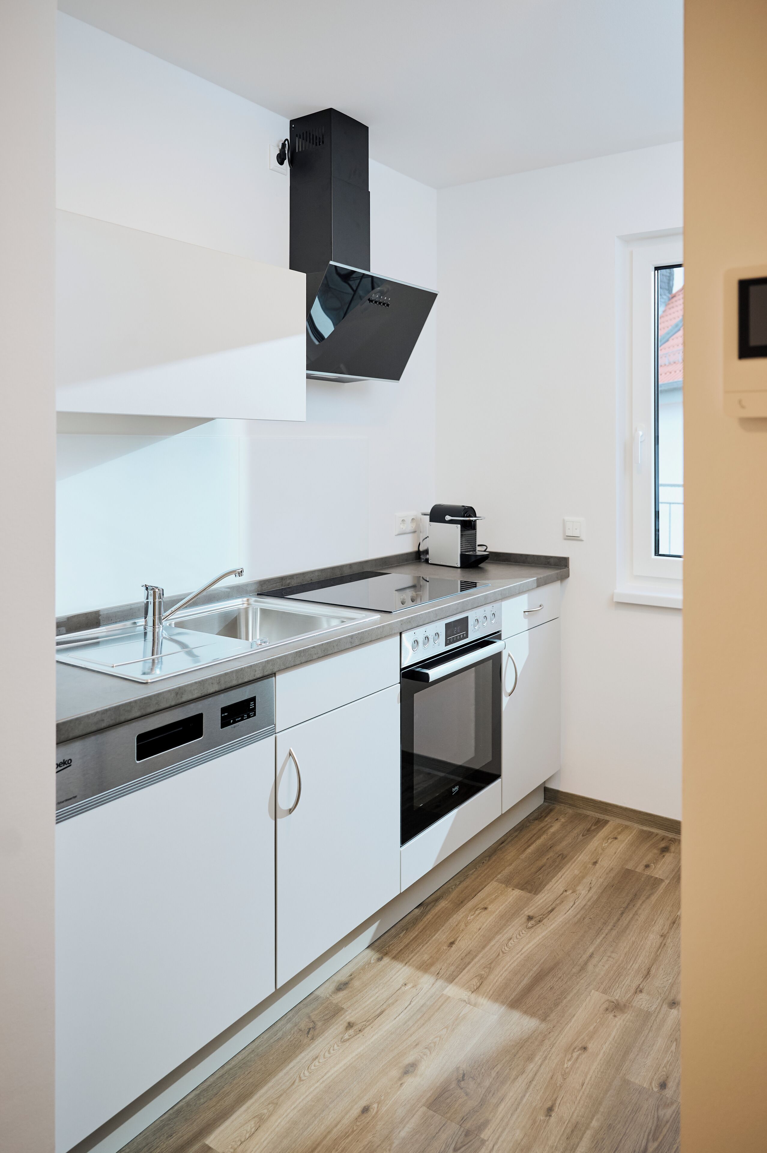 A modern kitchen with white cabinetry, a stainless steel sink, a built-in oven, and a window providing natural light.