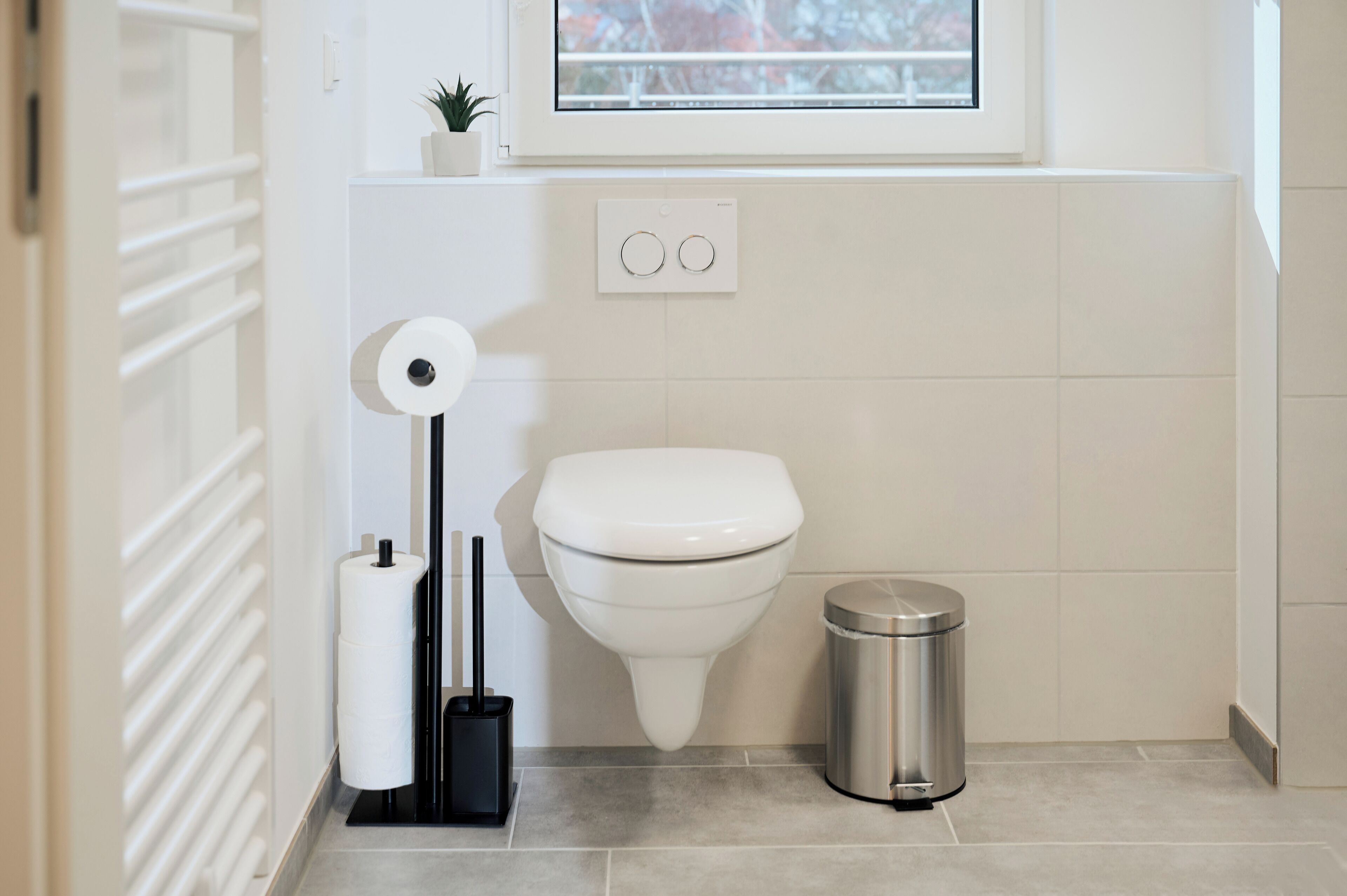 Une salle de bain moderne équipée de toilettes, d’un porte-rouleau de papier toilette, d’une poubelle et d’un radiateur.