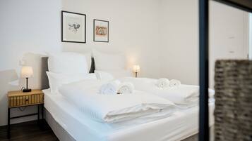 A neatly made bed with rolled towels, a bedside table with a lamp, and two framed artworks on the wall.