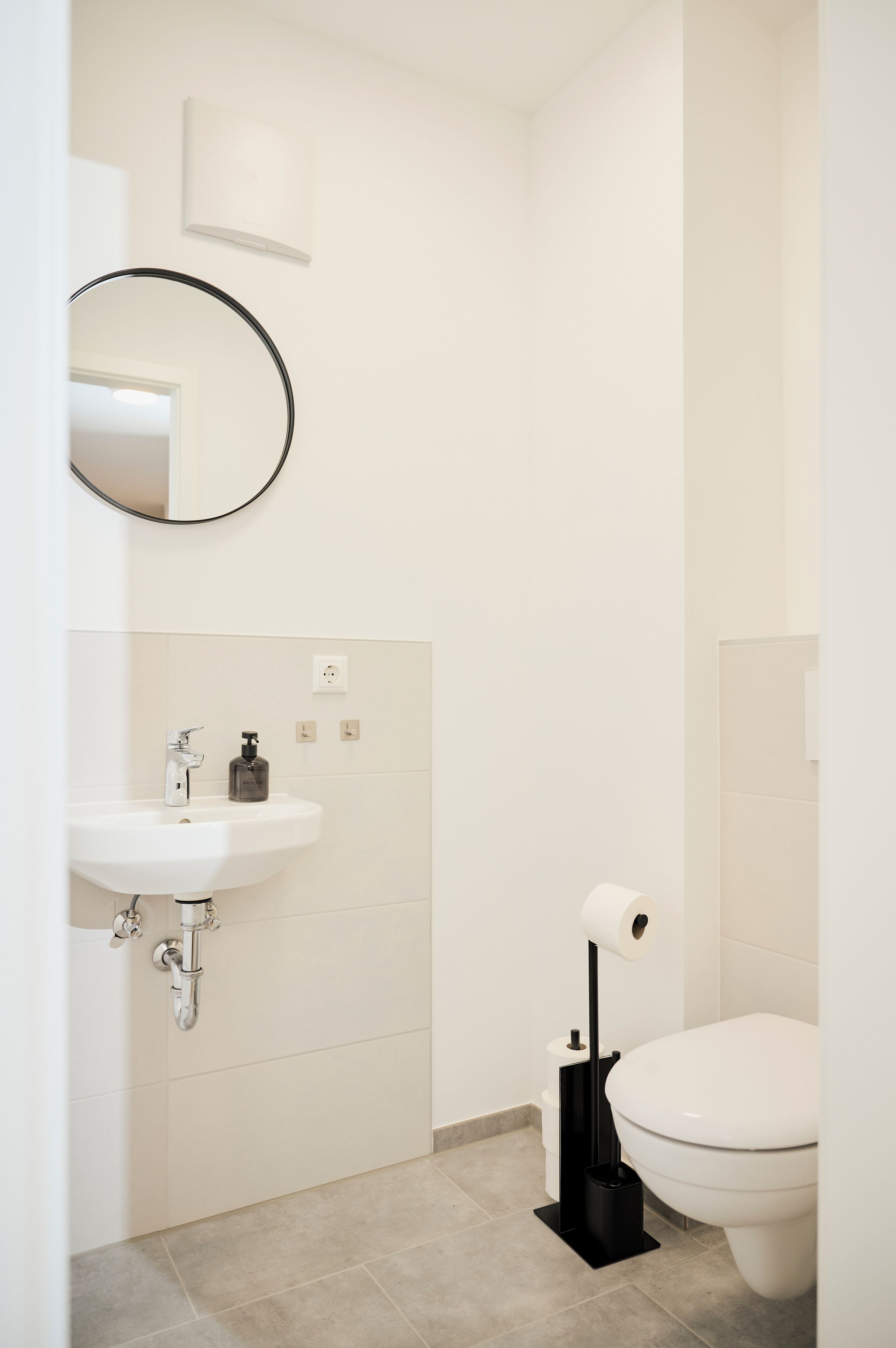 A modern bathroom with a white sink, toilet, and a black toilet brush.