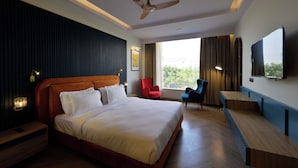 A hotel room with a large bed, a desk, a chair, a ceiling fan, and a TV mounted on the wall. - HOTEL THE PARK GATE (Mohali)